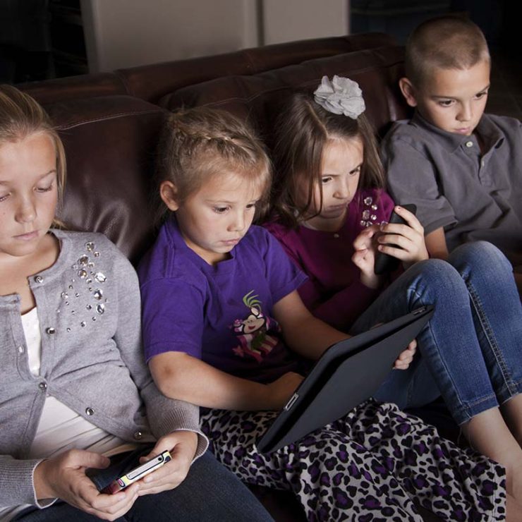 Kids on their tablets and phones sitting on the floor.