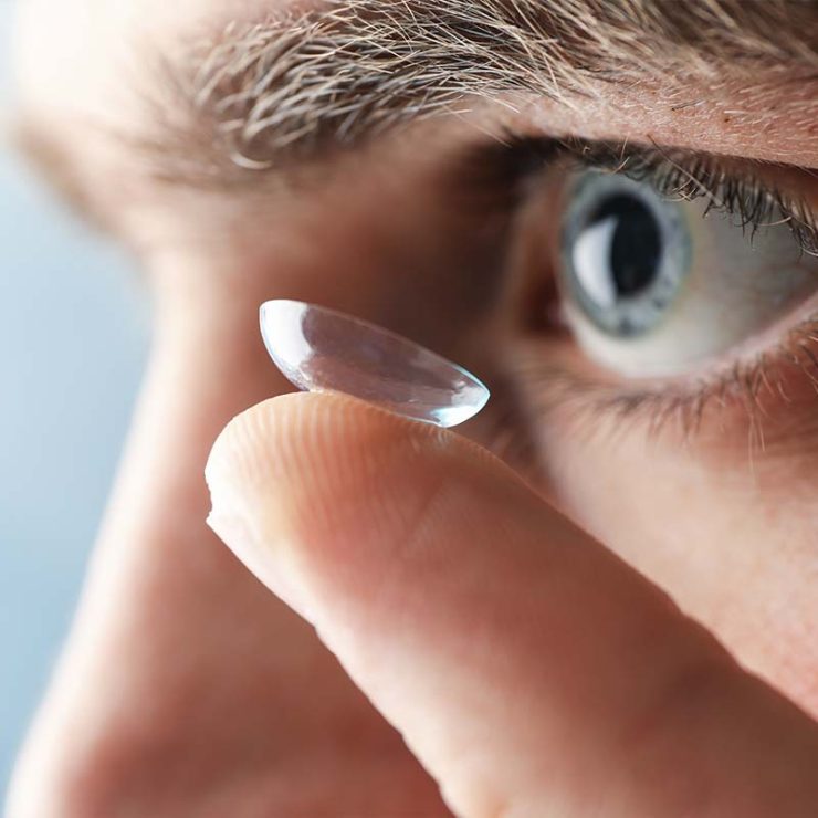 A close up of someone trying to put a contact lens into their eye.