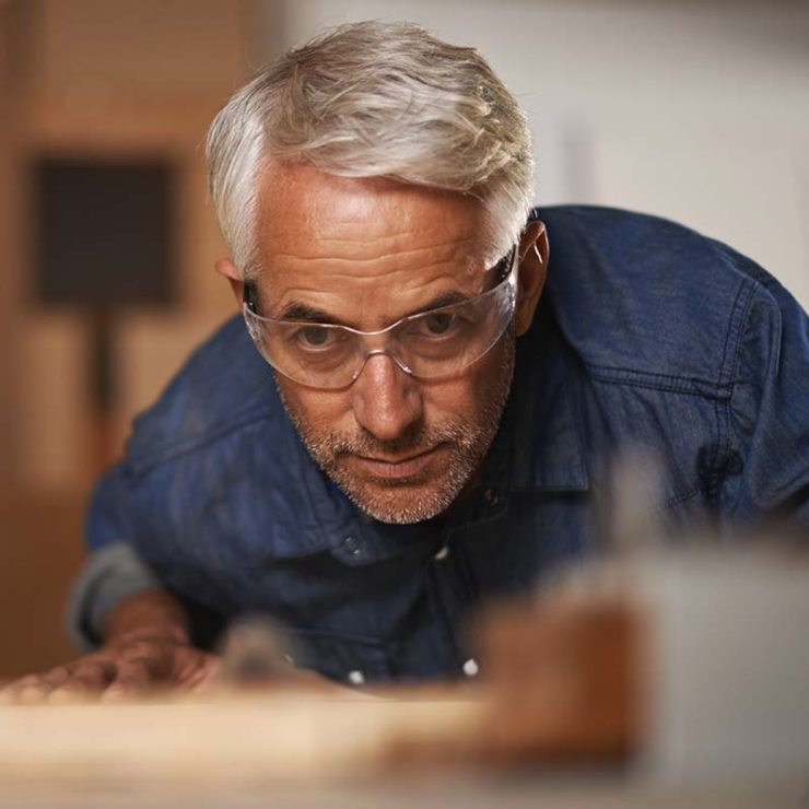 A man with white hair and denim shirt wearing prescription safety glasses.