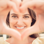 A smiling woman doing a heart shape for the camera.