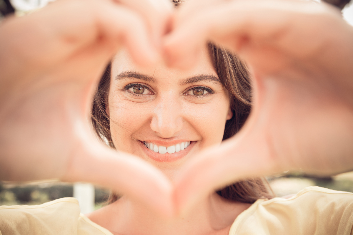 A smiling woman doing a heart shape for the camera.
