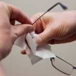 Hands cleaning a pair of glasses with wipes.
