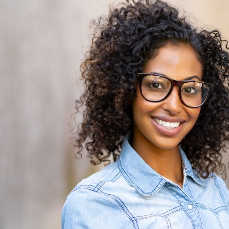 A beautiful curly woman wearing black glasses smiling.